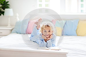 Child reading book in bed. Kids read in bedroom