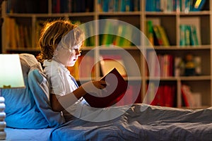 Child reading book in bed. Kids read at night