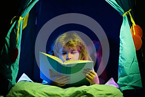 Child reading a book in the dark home. Kids bedtime. Boy read book in bed.