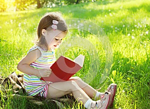 Child reading a book on the grass in sunny summer