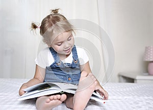 Child reading a book indoors.Caucasian kid reads a book sitting on a bed