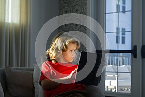 Child reading book at living room. Kids read books. Little boy sitting on couch in sunny living room watching pictures