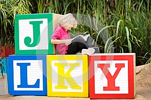 Child reading book in school yard. Kid learning abc letters. Little boy sitting on wooden toy blocks with alphabet in preschool or