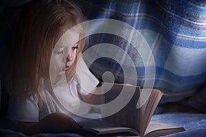 Child reading a book under the covers. Immersion into the magical world