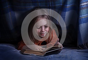 Child reading a book under the covers. Immersion into the magical world