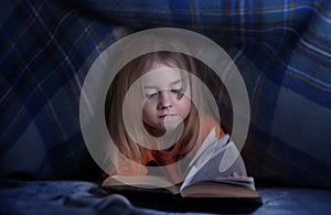 Child reading a book under the covers. Immersion into the magical world