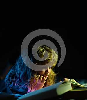 Child reading a magic book in bed. Kid boy read books at home. Concept of education and reading.