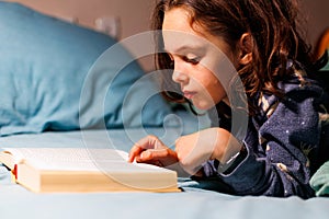 child reads a book before going to bed. Little curly boy in pajamas at home