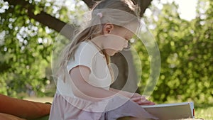 Child reads a book on the grass in a summer park. little girl leafs through a book on vacation