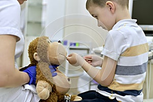 The child at the reception at the clinic examines the mouth cavity with a medical spatula of a toy plush monkey