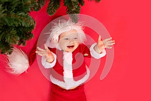A child on a red background in a Santa costume under the Christmas tree, the concept of new year and Christmas