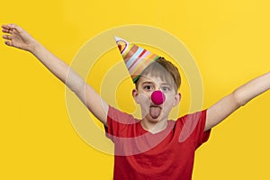 Child with red clown nose on yellow background. Cheerful clown boy. 1 April Fools day concept