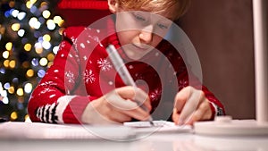 A child in a red sweater draws with markers on the background of Christmas lights
