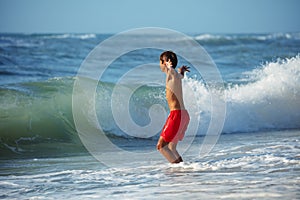 Child in red swim gear enjoys playful embrace of shoreline waves