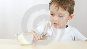 The child refuses to drink milk from a glass, close-up. Shooting on a white background.