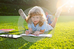 Child relax in the holiday. Kid with pencil writing on notebook on grass background. Nerd little genius, education and