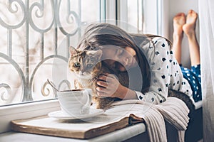 Child relaxing with a cat on a window sill