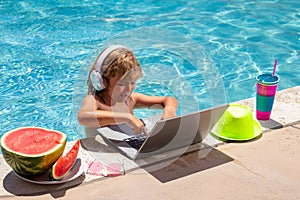 Child relaxing in the pool, using laptop computer in summer water. Kid boy online study or working on tropical sea beach