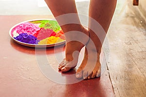 Child rests her legs on the floor beside a plate filled with holi powders