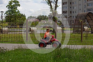 A child rides an electric quad bike in the summer in the park. During the holidays, the boy and his family rented an