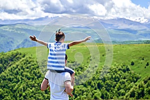 the child rides on the shoulders of his father with his arms spread out. summer of the mountain. fresh air. rest