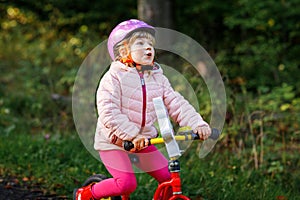 Child riding balance bike. Kids on bicycle in sunny forest. Little girl enjoying to ride glider bike on warm day