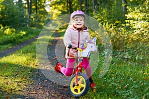 Child riding balance bike. Kids on bicycle in sunny forest. Little girl enjoying to ride glider bike on warm day