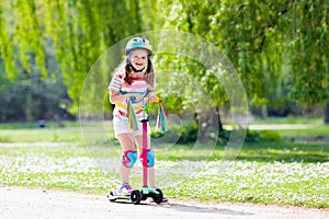 Child riding kick scooter in summer park.