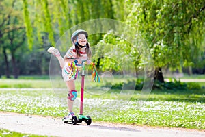 Child riding kick scooter in summer park.