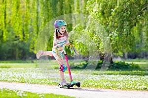 Child riding kick scooter in summer park.