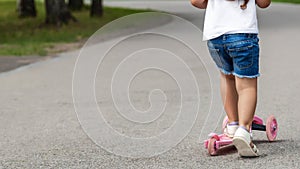 Child riding scooter. Happy little kid girl playing pink kick board on road in park outdoors on summer day, Active children games