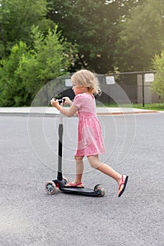 Child riding scooter. Little girl spending time outdoor in summer