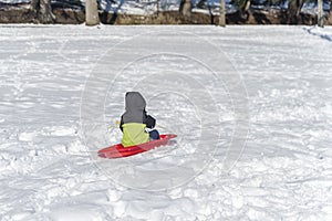 Child is riding a toboggan from the mountain on white snow