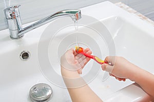 The child rinses toothbrush under running water photo