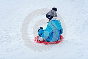 child rolls down a snow hill. Boy sliding down snow hill in winter. Kids play outside. Winter fun concept
