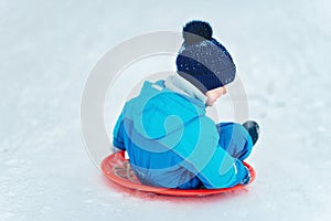 Child rolls down a snow hill. Boy sliding down snow hill in winter. Kids play outside. Winter fun concept