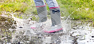 A child in rubber boots jumps in a puddle