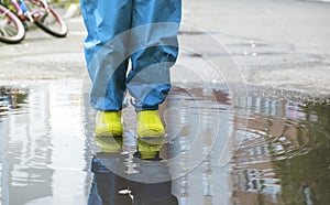 a child in rubber boots and waterproof pants stands in a puddle, his legs close-up.