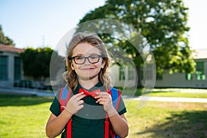 Child with rucksacks in the school park. Pupils with backpacks outdoors. Nerd pupil ties a bowtie, correcting red bow