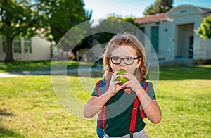 Child with rucksacks in the school park. Pupils with backpacks outdoors. Schoolboy eating apple.