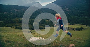 Child run on mountain meadow at rainy day with low clouds on sky in rubber boots