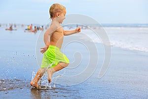 Child run with splashes by water pool along sea surf