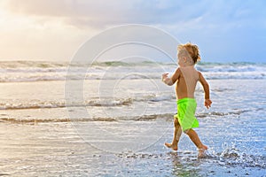 Child run with splashes by water pool along sea surf