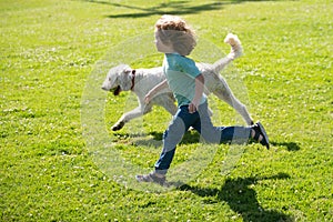 Child runnin with a dog in park. Kid with a puppy dog outdoor playing at backyard lawn.