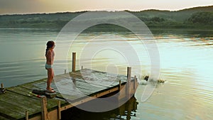 Child running and jumping off pier in lake water on the Sunset. Slow motion.