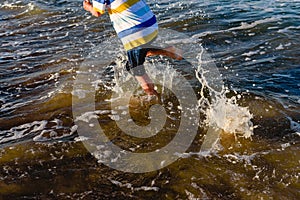 Child running on the sand of the beach splashing with waves in summer