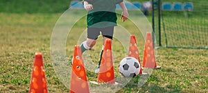 Child running soccer ball between training cones. European football sports summer camp for junior level athletes