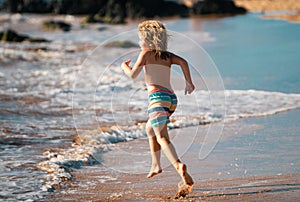 Child running through water close to shore along the sea beach. A boy runs along the sea coast. Rest of children on