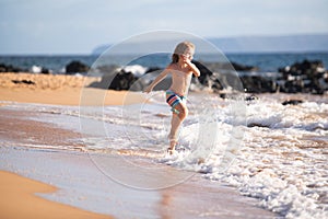 Child running through water close to shore along the sea beach. A boy runs along the sea coast. Rest of children on