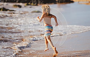 Child running through water close to shore along the sea beach. A boy runs along the sea coast. Rest of children on